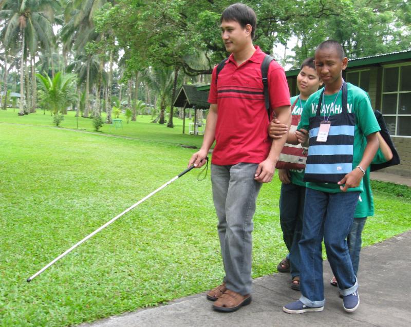 Blind camp instructor with cane leads other blind students